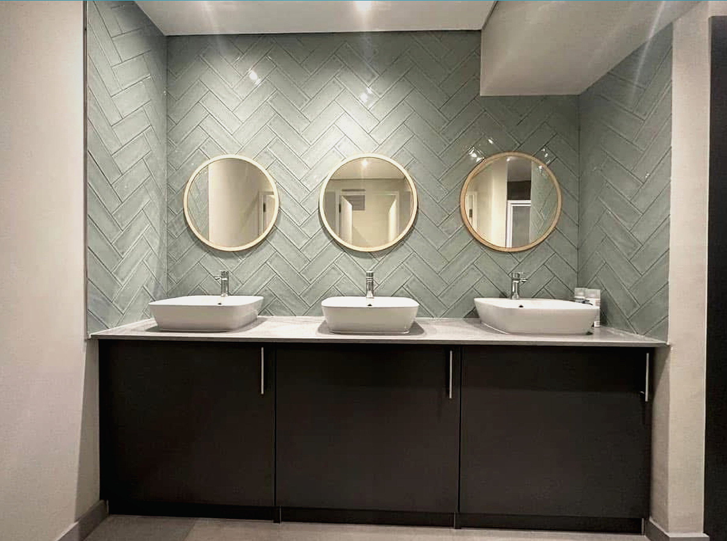 A bathroom with three basins, round mirrors and herringbone wall tiles