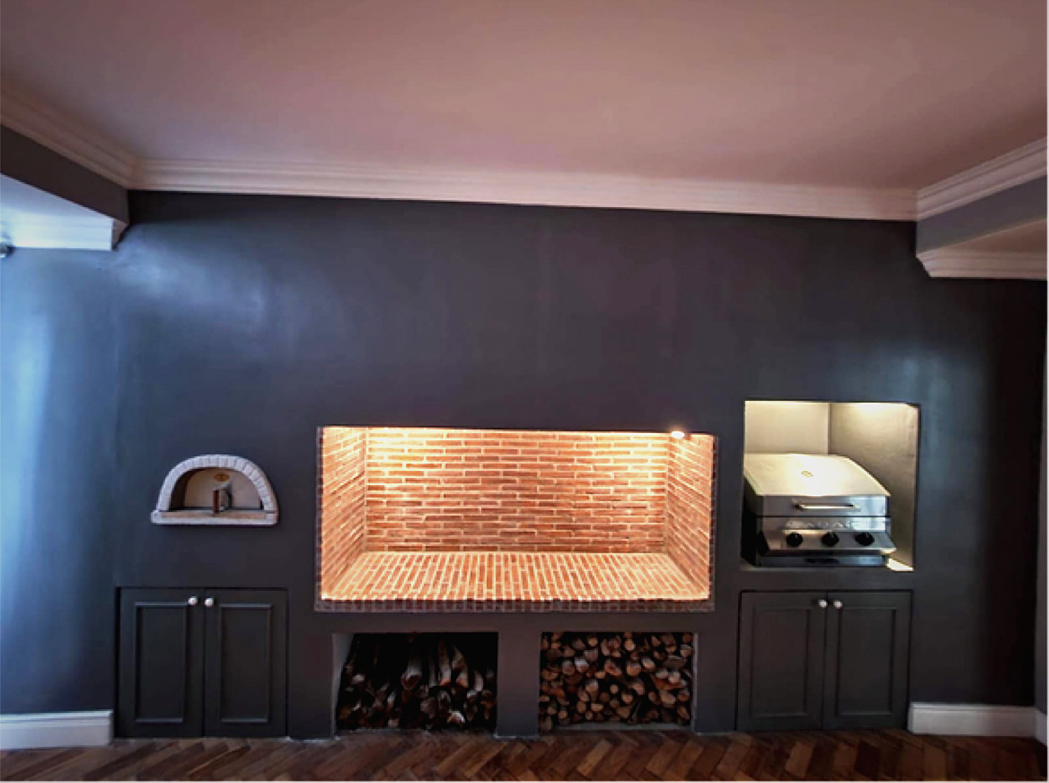 A braai room after renovation: charcoal walls, a lit brick braai, built-in cupboards and a herringbone floor