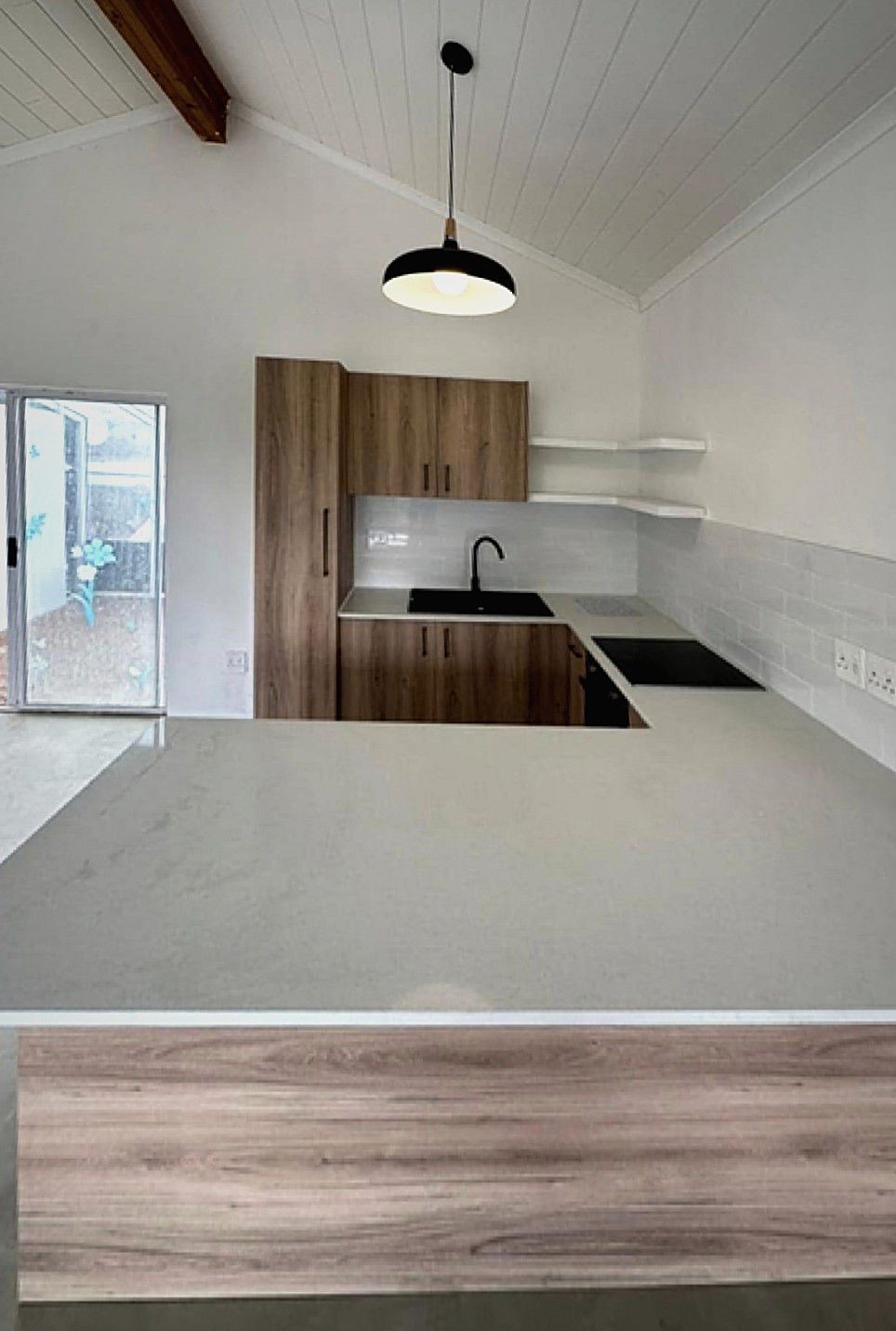 A renovated kitchen with a white ceiling, pendant light, wood-grain units and a stone counter